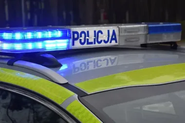 Zbliżenie na dach policyjnego radiowozu z włączonym niebieskim światłem i napisem POLICJA.